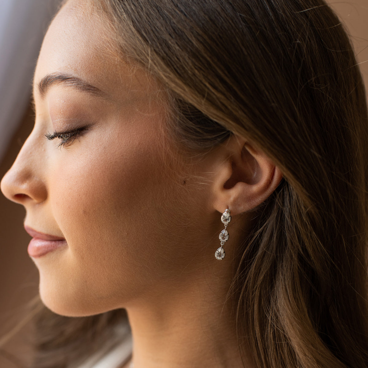 Harmony Drop Hoop Earrings - White Topaz Woman wearing a pearl necklace and earrings with a neutral background