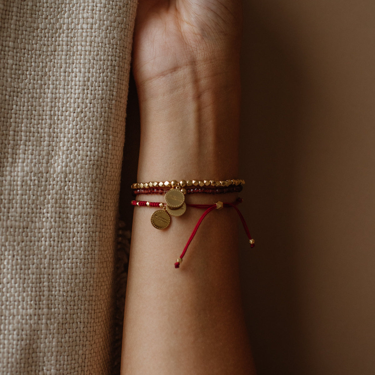 Close-up of a wrist wearing multiple bracelets on a neutral background