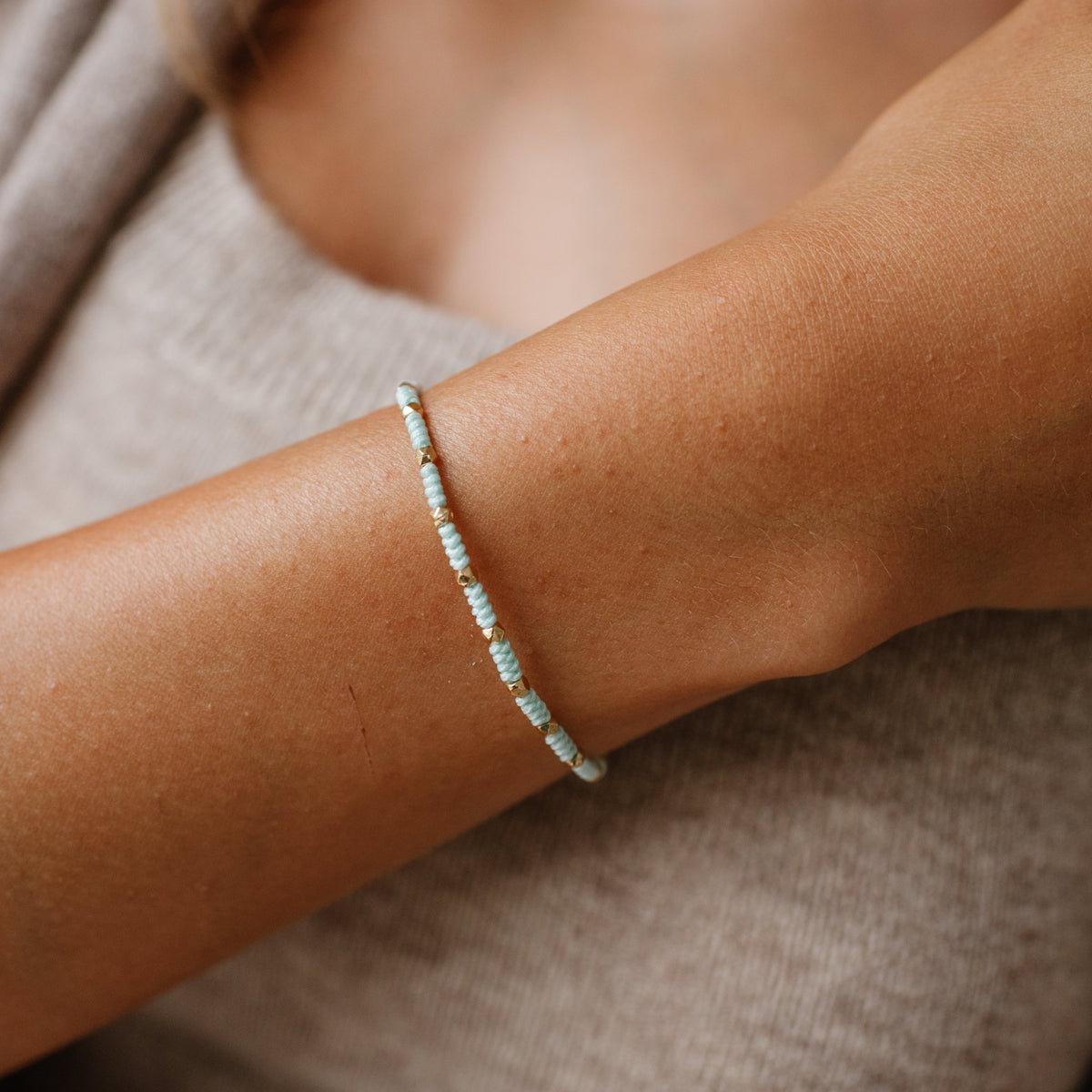 Close-up of a wrist wearing a delicate bracelet with a neutral background