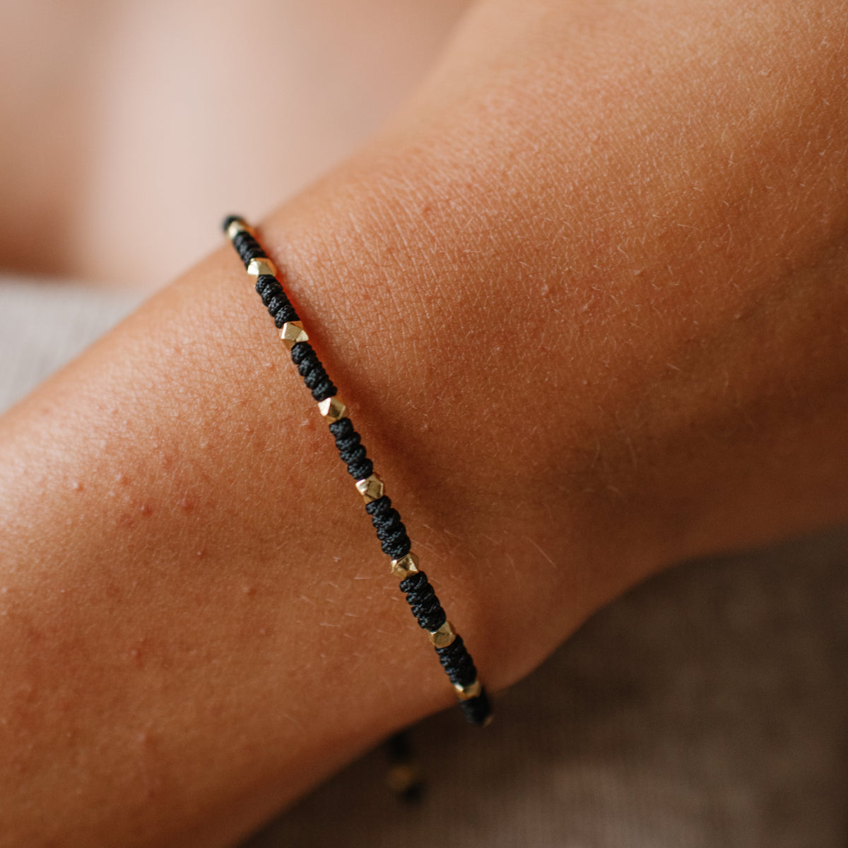 Close-up of a wrist wearing a black beaded bracelet on a neutral background