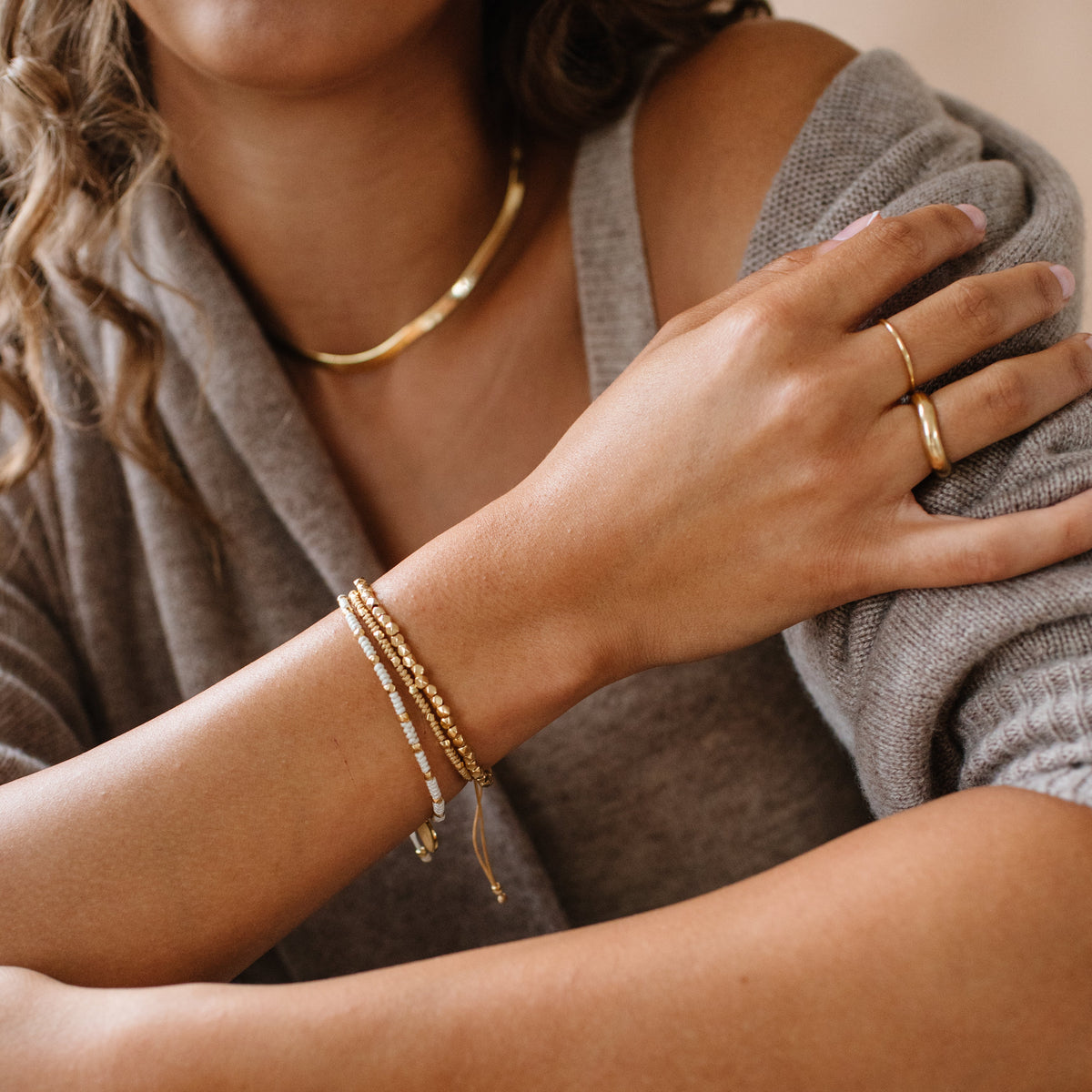 Close-up of a person wearing gold jewelry including a necklace, bracelet, and ring.