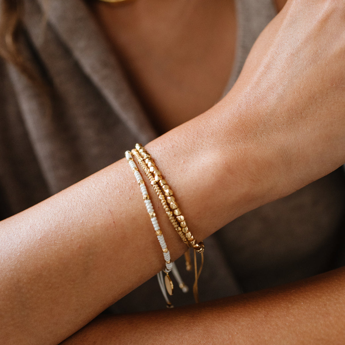 Close-up of a person&#39;s wrist wearing gold bracelets on a neutral background