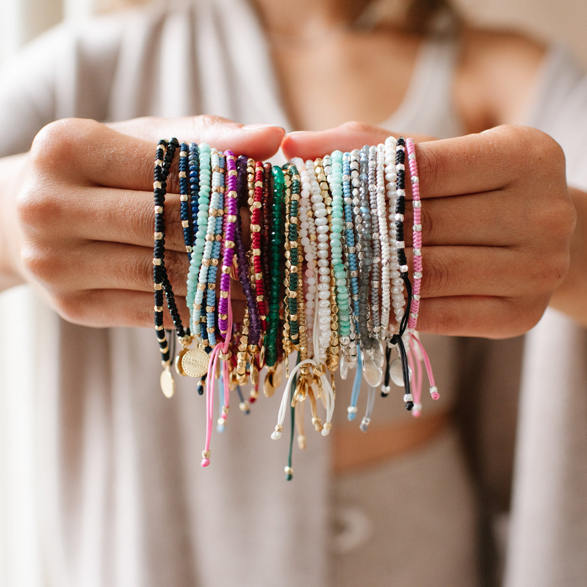 Person holding colorful bracelets in front of a neutral background