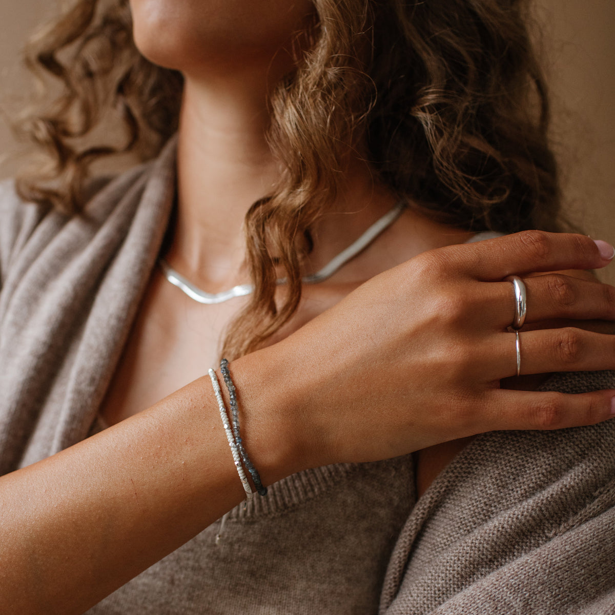 Woman wearing jewelry including a necklace, bracelet, and ring, with a neutral background.