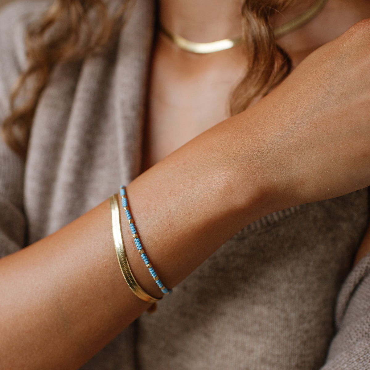 Close-up of a person wearing gold bracelets on a neutral background