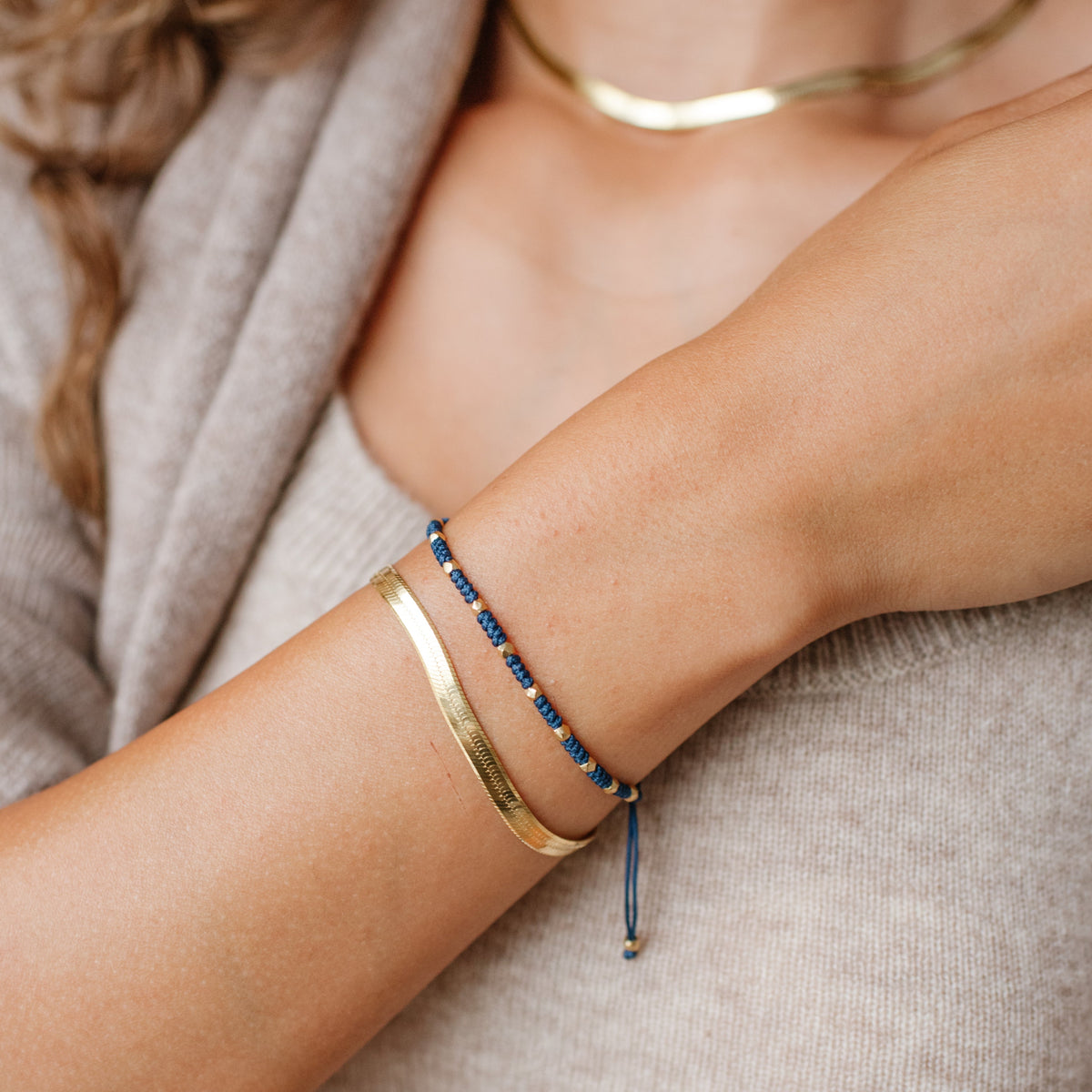 Close-up of a person&#39;s arm wearing gold and blue bracelets on a neutral background