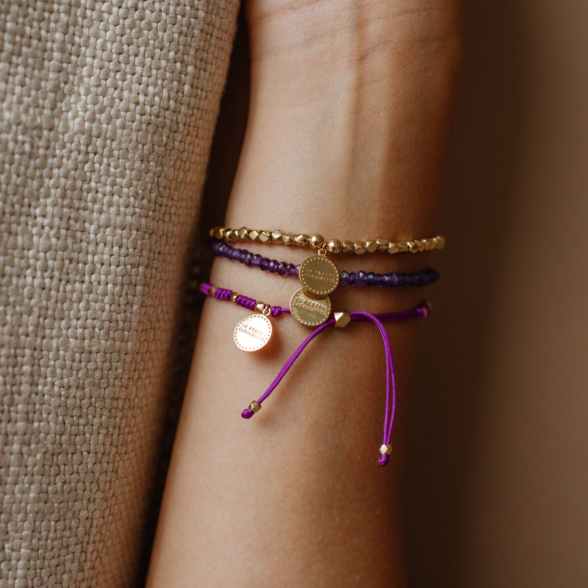 Purple bracelet with a small round charm on a wrist against a neutral background