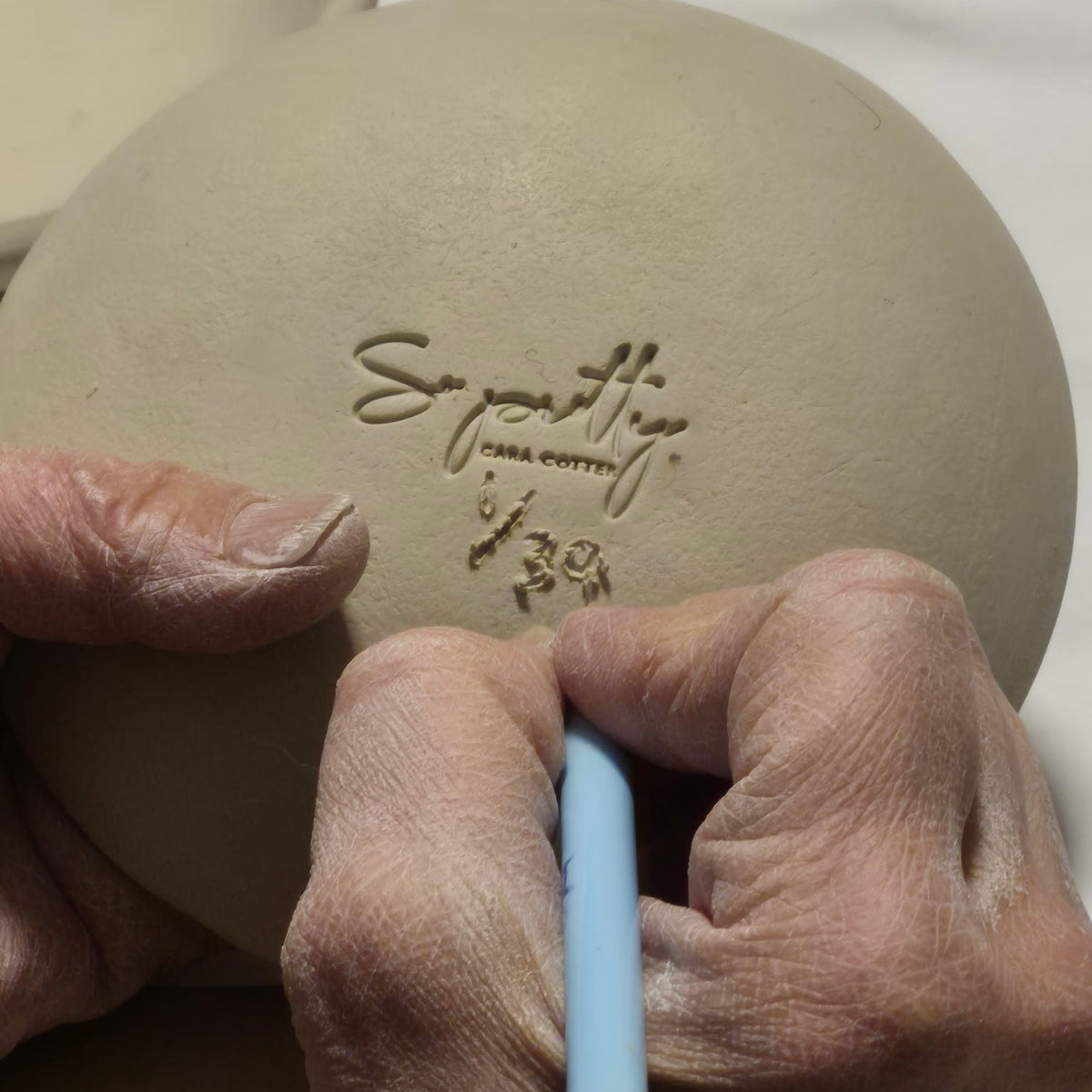 Hands holding a ceramic product with branding on a white background