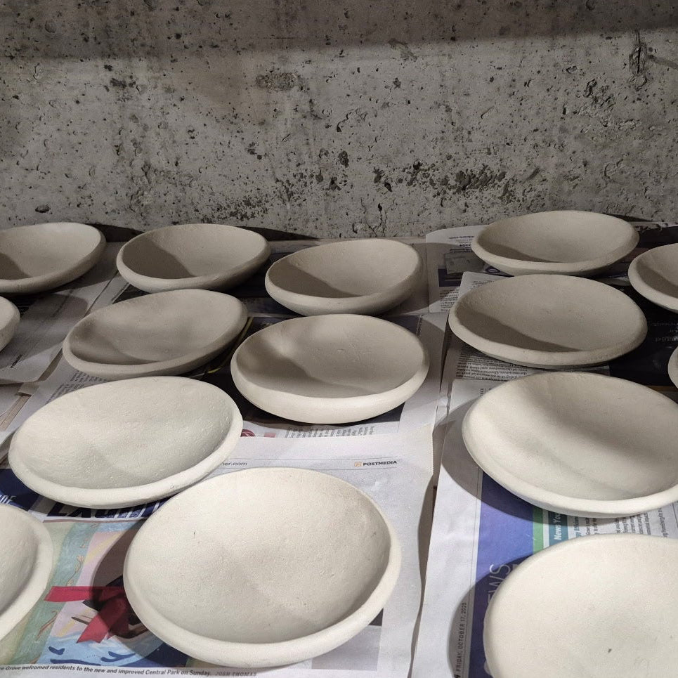 Row of ceramic bowls on a newspaper with a concrete wall background