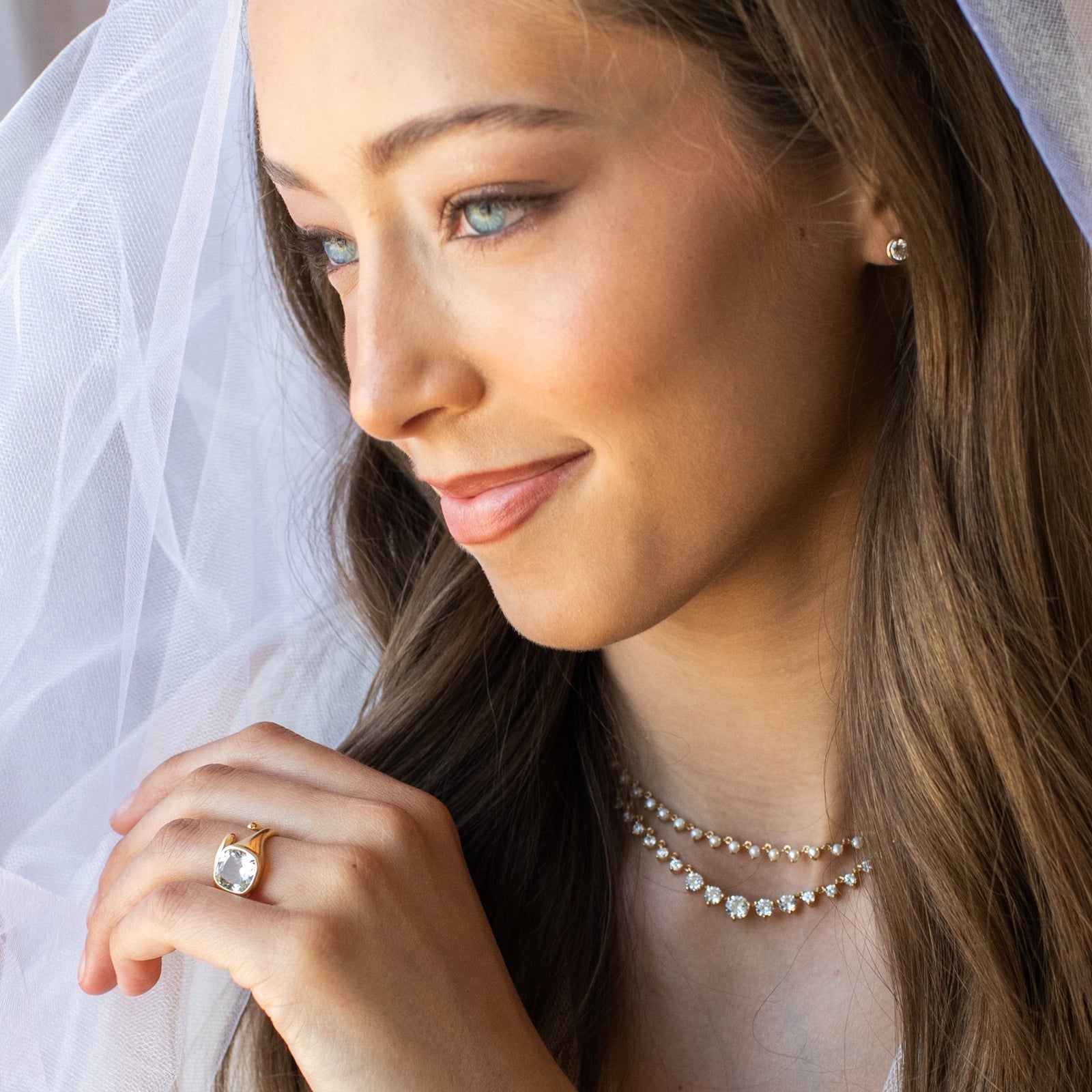 Woman wearing a wedding ring and pearl jewelry with a veil in the background