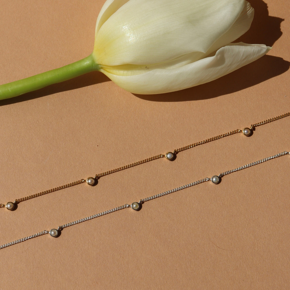 Two pearl necklaces on a beige surface with a white tulip.