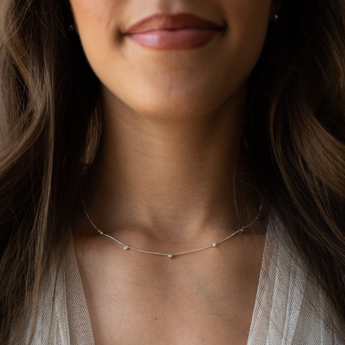 Close-up of a woman wearing a delicate necklace with a soft focus on her face and shoulders.