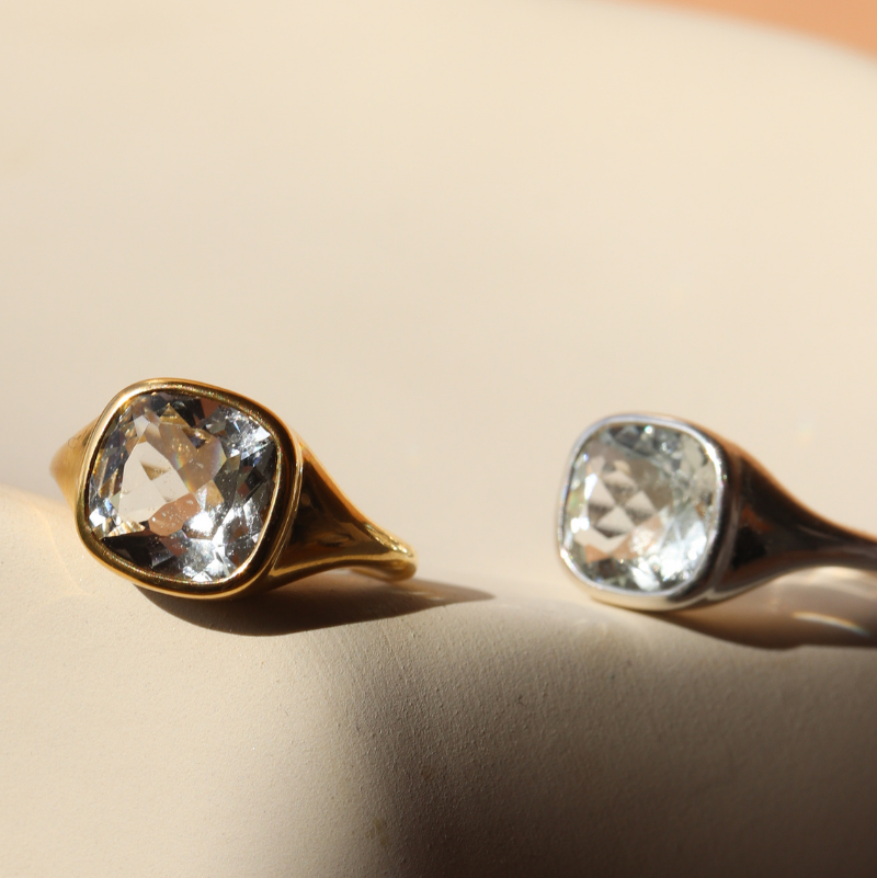 Two gold rings with clear gemstones on a beige background